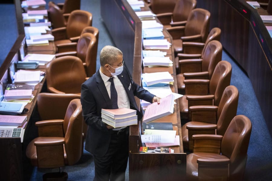 An usher distributes the planned state budget on the tables of MKs during a plenum session ahead of the vote, Nov. 2, 2021. (Photo: Olivier Fitoussi/Flash90)