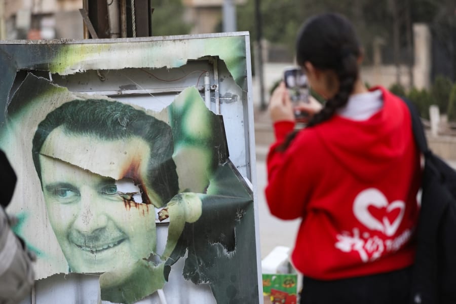 Une femme utilise son téléphone portable près d'une photo endommagée du président syrien Bashar al-Assad alors que les gens célèbrent, après que les rebelles syriens aient annoncé qu'ils ont chassé le président Bashar al-Assad, à Qamishli, Syrie le 8 décembre 2024. (Photo : REUTERS/Orhan Qereman)
