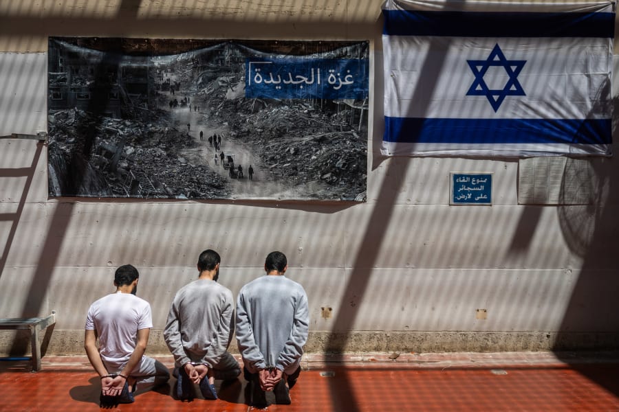 Des terroristes du Hamas menottés sont assis à côté d'une photo de Palestiniens passant devant des bâtiments détruits dans la bande de Gaza et d'un drapeau israélien, dans une prison du centre d'Israël, le 6 mai 2025. (Photo : Chaim Goldberg/Flash90)