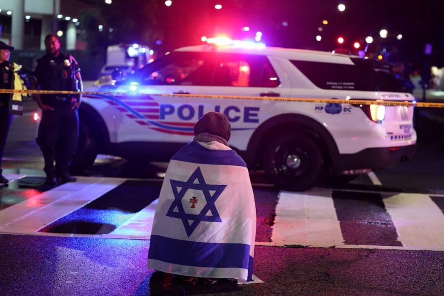 A man, with an Israeli flag with a cross in the center, kneels next to emergency personnel working at the site where, according to the U.S. Homeland Security Secretary, two Israeli embassy staff were shot dead near the Capital Jewish Museum in Washington, D.C., U.S. May 21, 2025. REUTERS/Jonathan Ernst