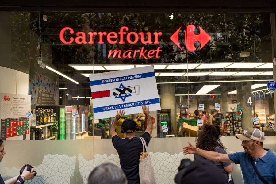 A man holds a placard in front of a Carrefour supermarket during a protest against Israel, June 14, 2025, Barcelona, Spain. (Photo: Davide Bonaldo / SOPA Images via Reuters)