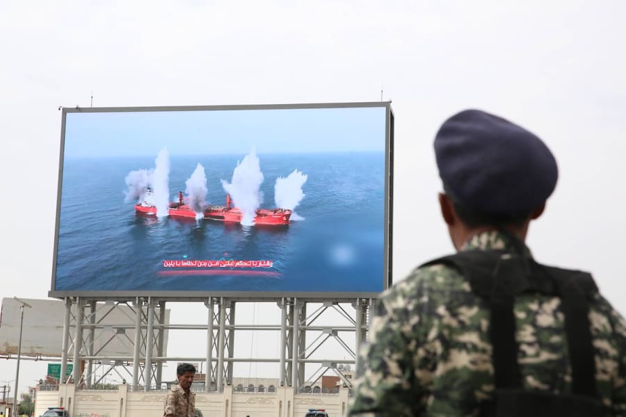 Боец-хусит стоит на страже перед цифровым билбордом, показывающим клубы дыма, поднимающиеся от атакованного хуситами судна в Красном море, Сана, Йемен, 25 июля 2025 года. (Фото: IMAGO/Hamza Ali via Reuters)