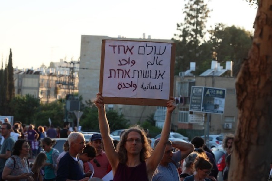 A man holding a sign in Hebrew and Arabic "One world, one humanity" (Photo: Sharona Weiss)