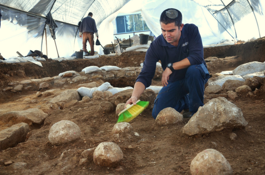 Kfir Arbiv, Israel Antiquities Authority excavation director, cleans a ballista stone. (Photo: Yoli Schwartz/Israel Antiquities Authority)