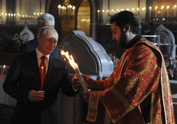 Russian President Vladimir Putin takes lighted candles from a priest during an Orthodox Easter service in the Christ the Saviour Cathedral in Moscow, April 20, 2014. (Photo:REUTERS/Mikhail Klimentyev/RIA Novosti/Kremlin)