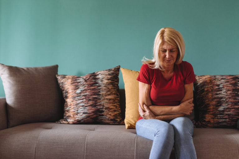 Lady sitting on couch bent over in stomach pain | HealthMasters
