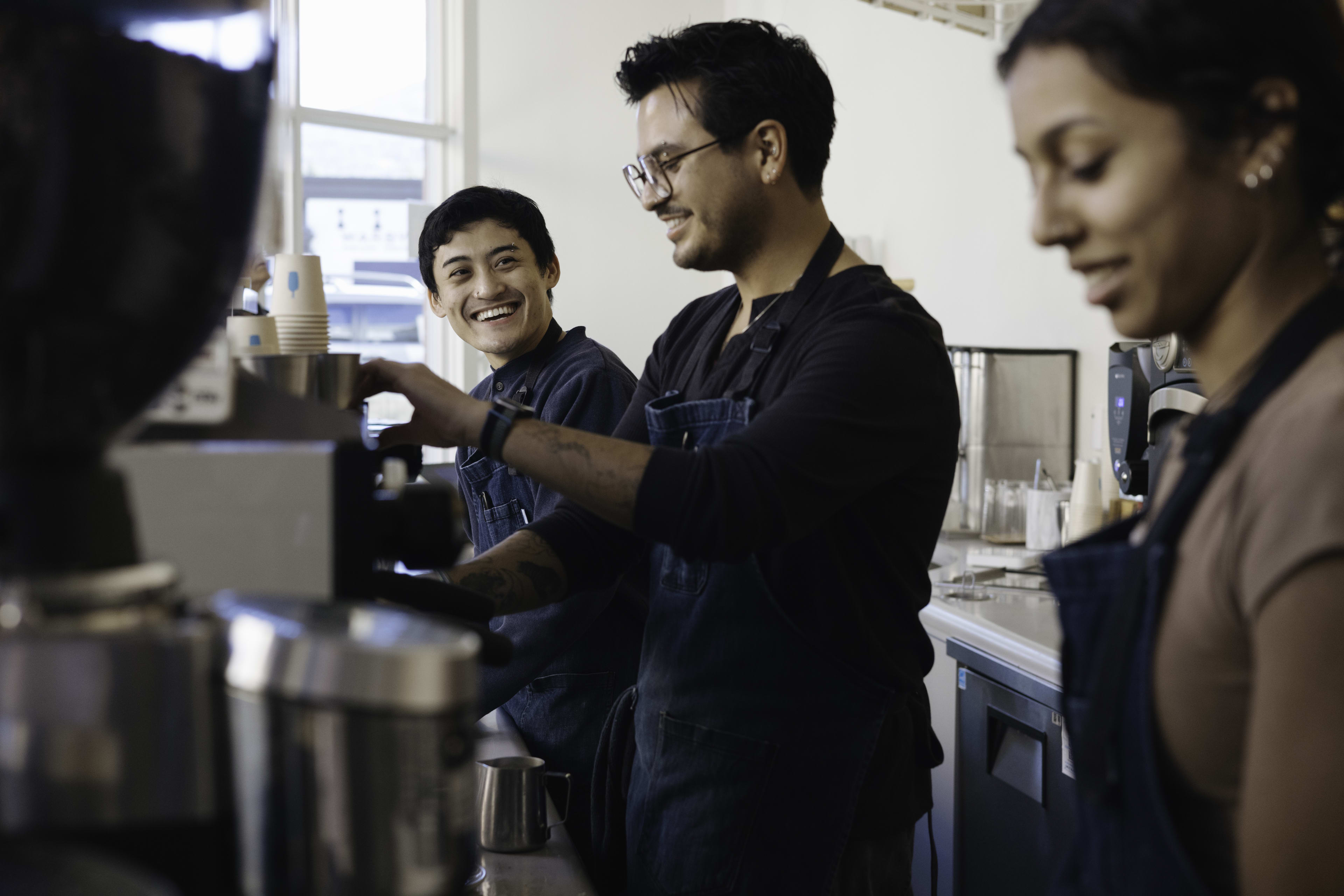 two baristas smile at each other while working at the espresso machine
