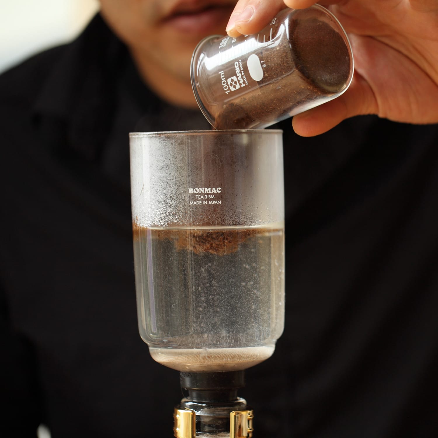 Ground coffee being added to the top chamber of the siphon.