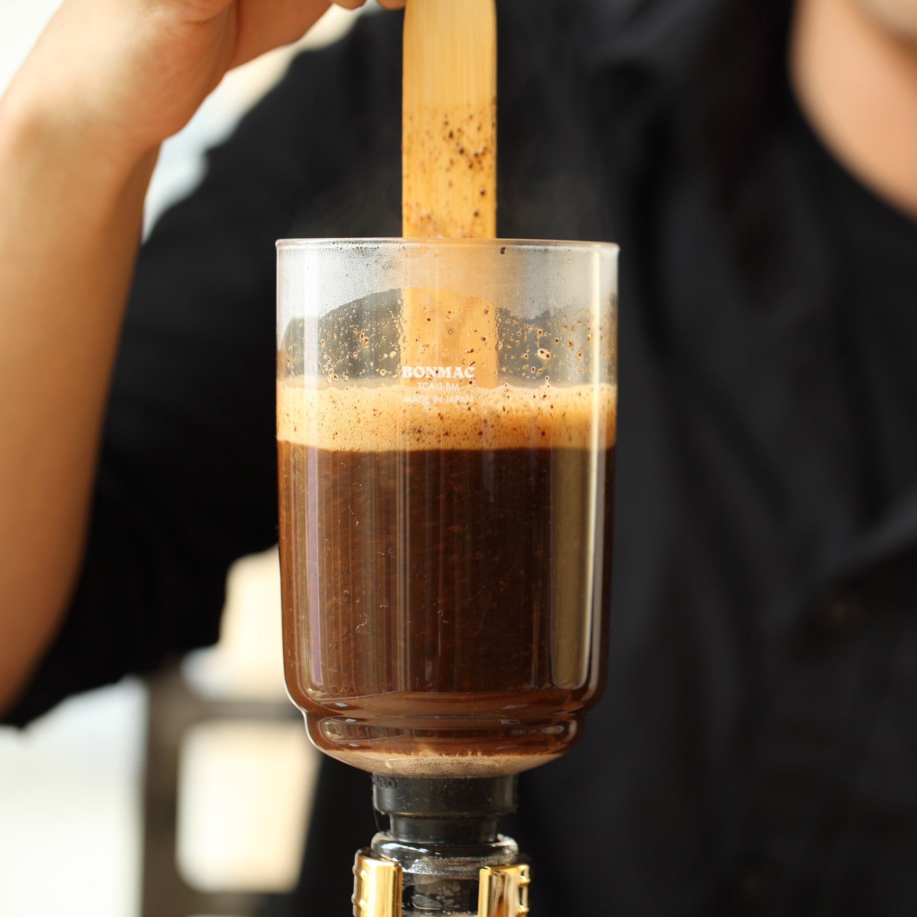 Coffee in the top chamber of a siphon being stirred.