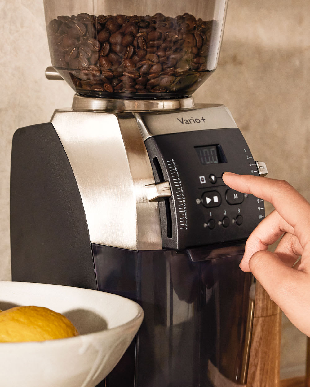 A person adjusting the setting of the Baratza Vario+ Home Coffee Grinder.