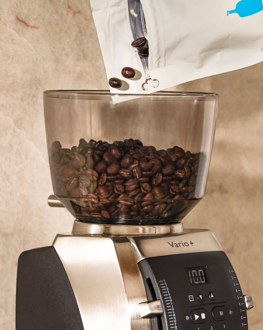 Coffe beans being poured into the hopper of the A person adjusting the setting of the Baratza Vario+ Home Coffee Grinder.