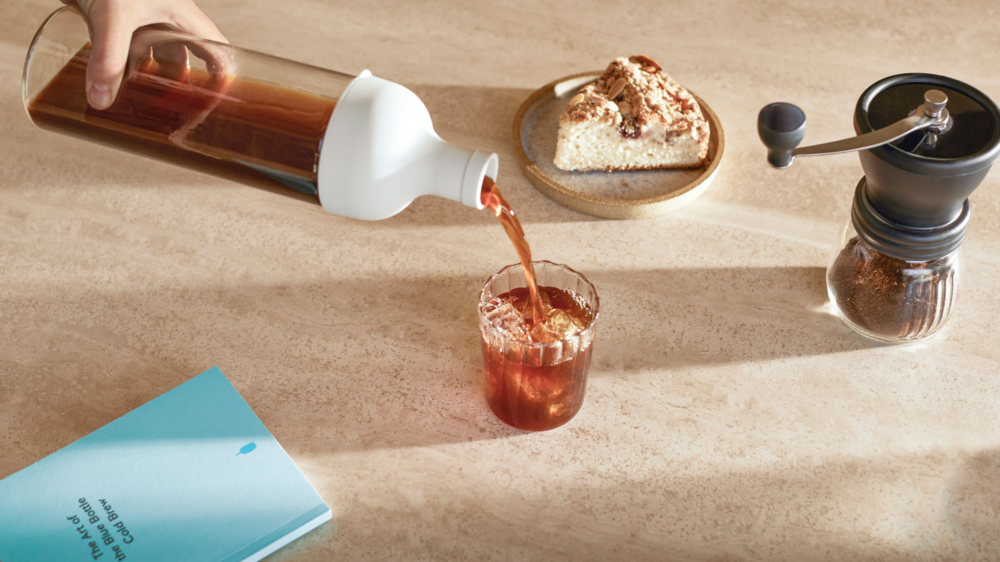 Image of cold brew kit items in use; someone is pouring coffee from the Hario cold brew bottle into a glass with ice.