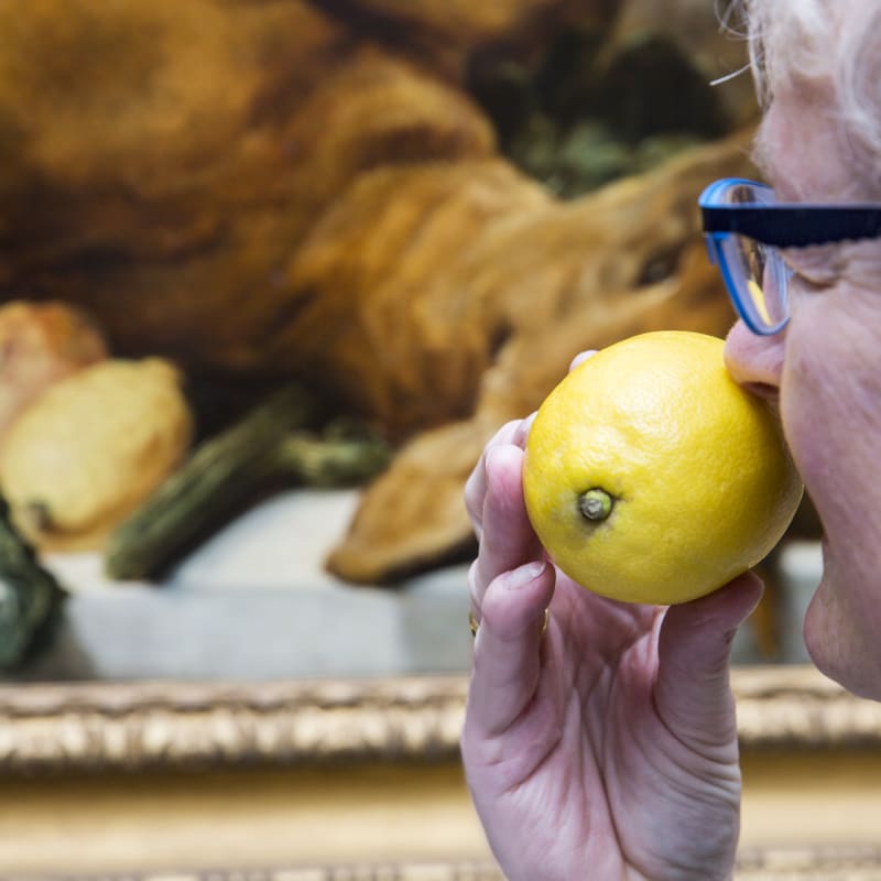 Eine Frau mit einer Zitrone vor einem Gemälde. 