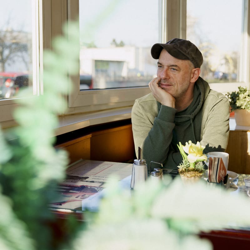 Autor Stephan Lose sitzt in einem Café. Er guckt freudnlich an der Kamera vorbei.