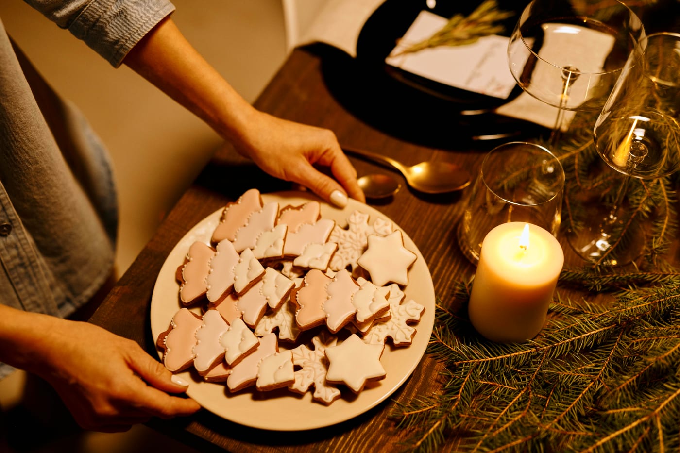 Christmas arrangement with star-shaped cookies on a dish, surrounded by candles and fir branches on a table, creating a warm and inviting atmosphere.