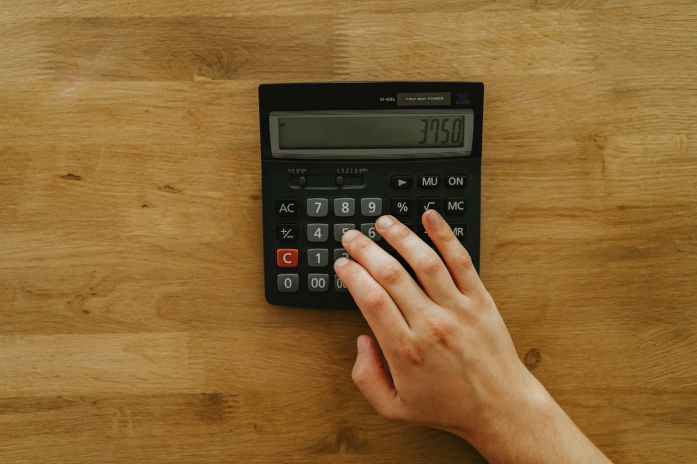 Hand using budget calculator on wooden table for confirmation planning.