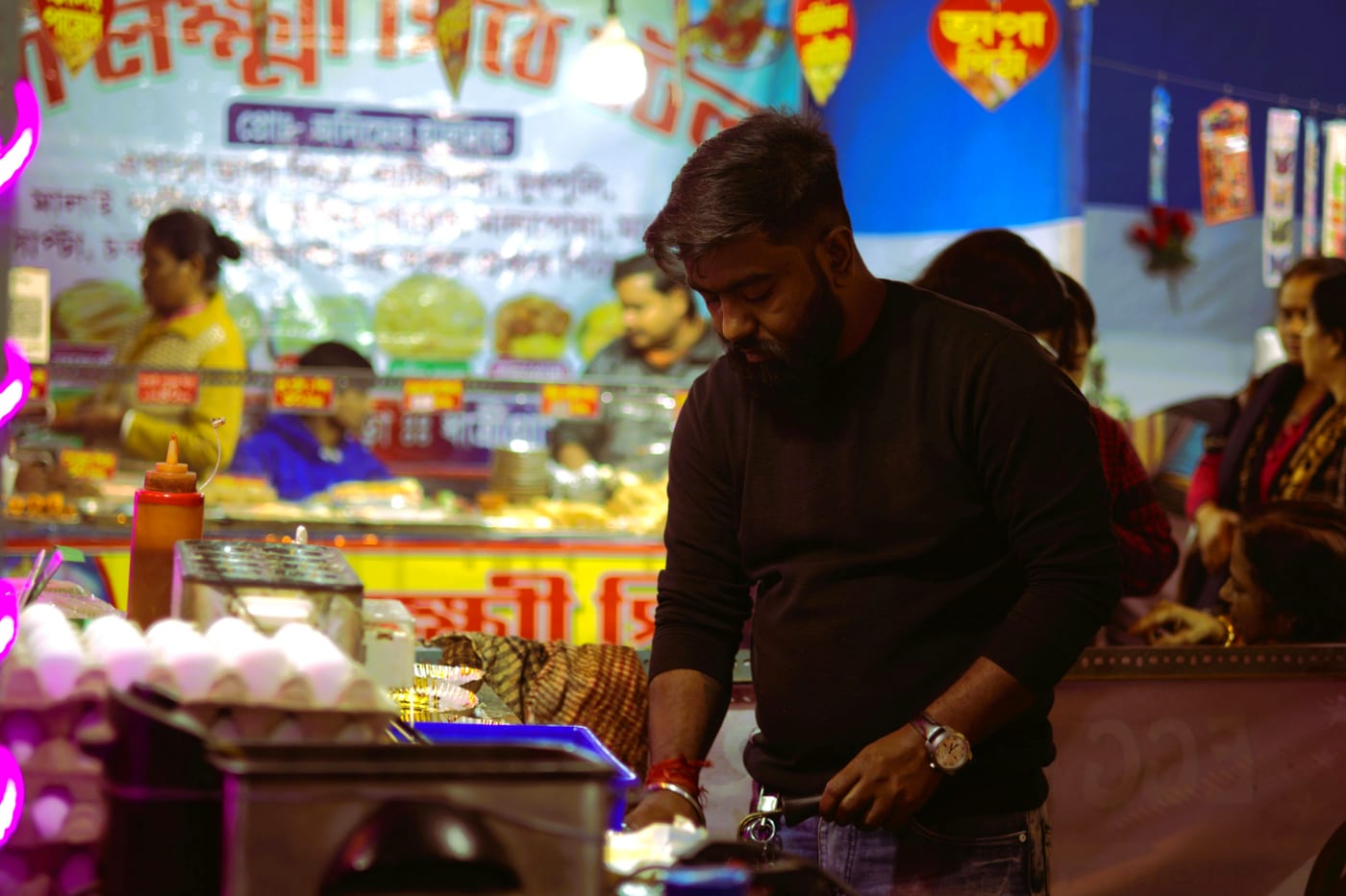 Street vendor preparing street food at a lively food festival with neon lights and colorful signs, creating an authentic atmosphere.