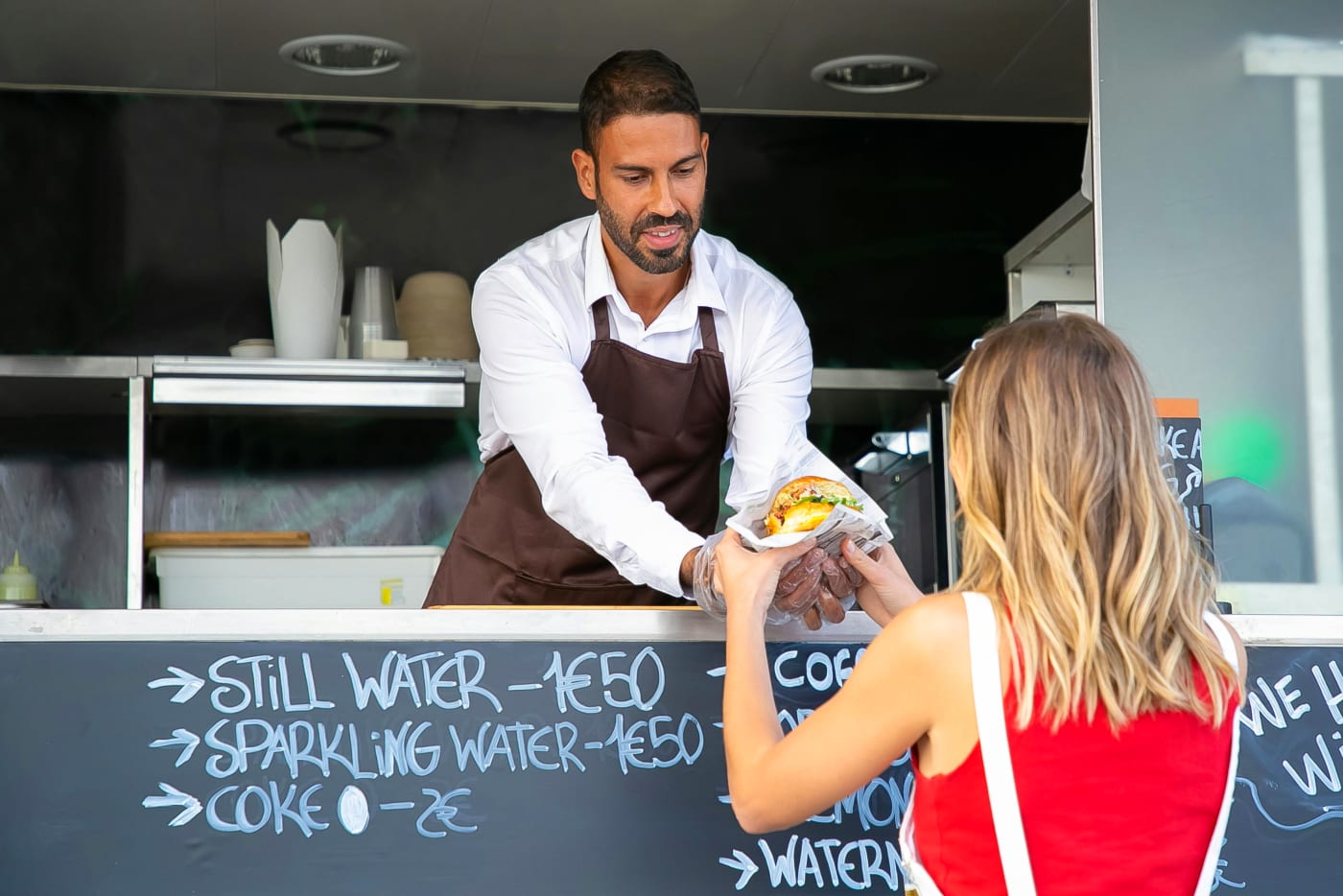 Street food vendor serving diverse street food from a food truck, with menu signage.
