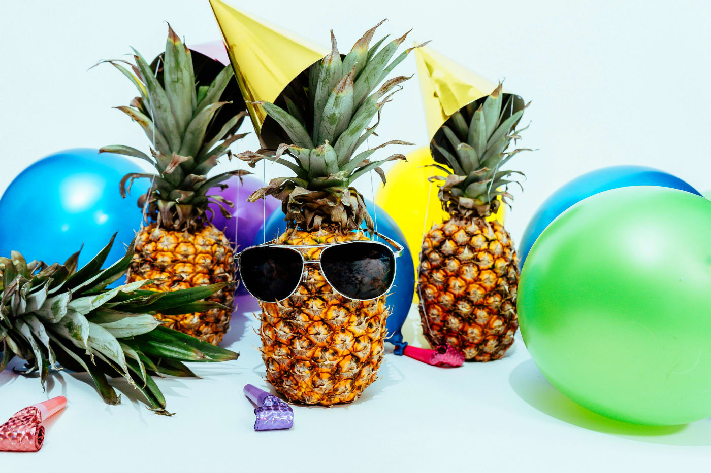 Colorful pineapples with sunglasses and festive hats surrounded by balloons, capturing the lively atmosphere of a street food party.