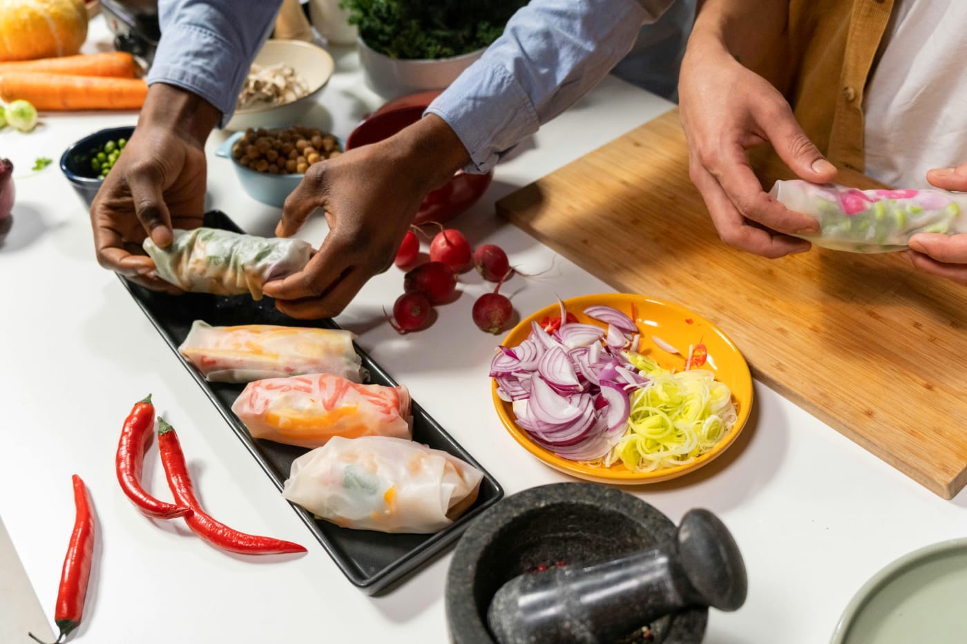 People making appetizers with fresh, colorful vegetables and creative wraps, surrounded by radishes and chili.