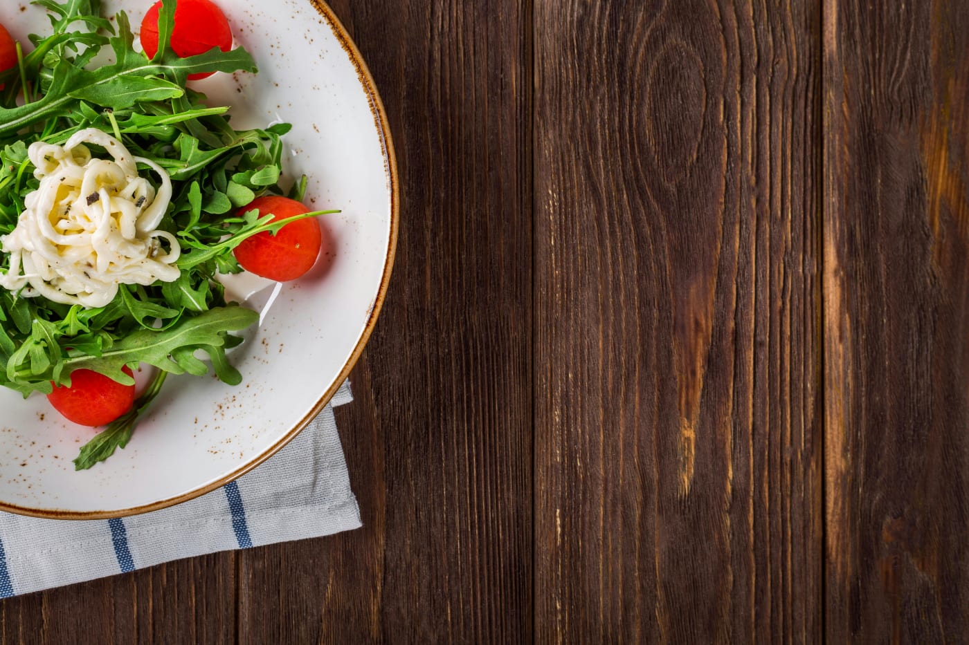 Fresh salad with arugula, tomatoes, and cheese on a rustic wooden table as part of a vegetarian party menu.