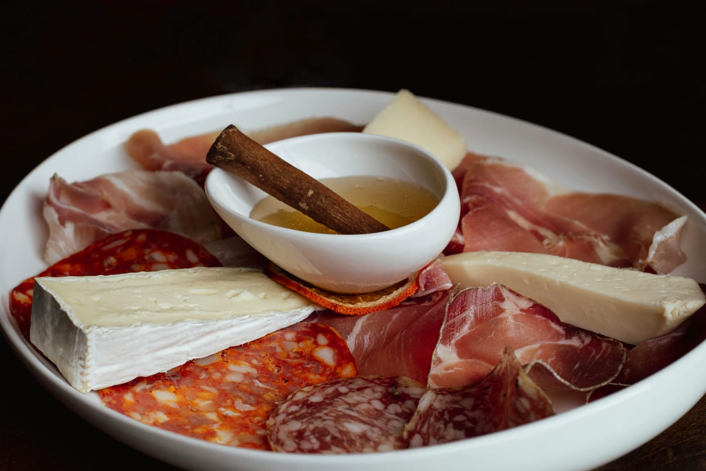 Assorted selection of Spanish tapas with charcuterie, cheese, and a small bowl of honey on a white plate, perfect for social sharing and enjoyment.