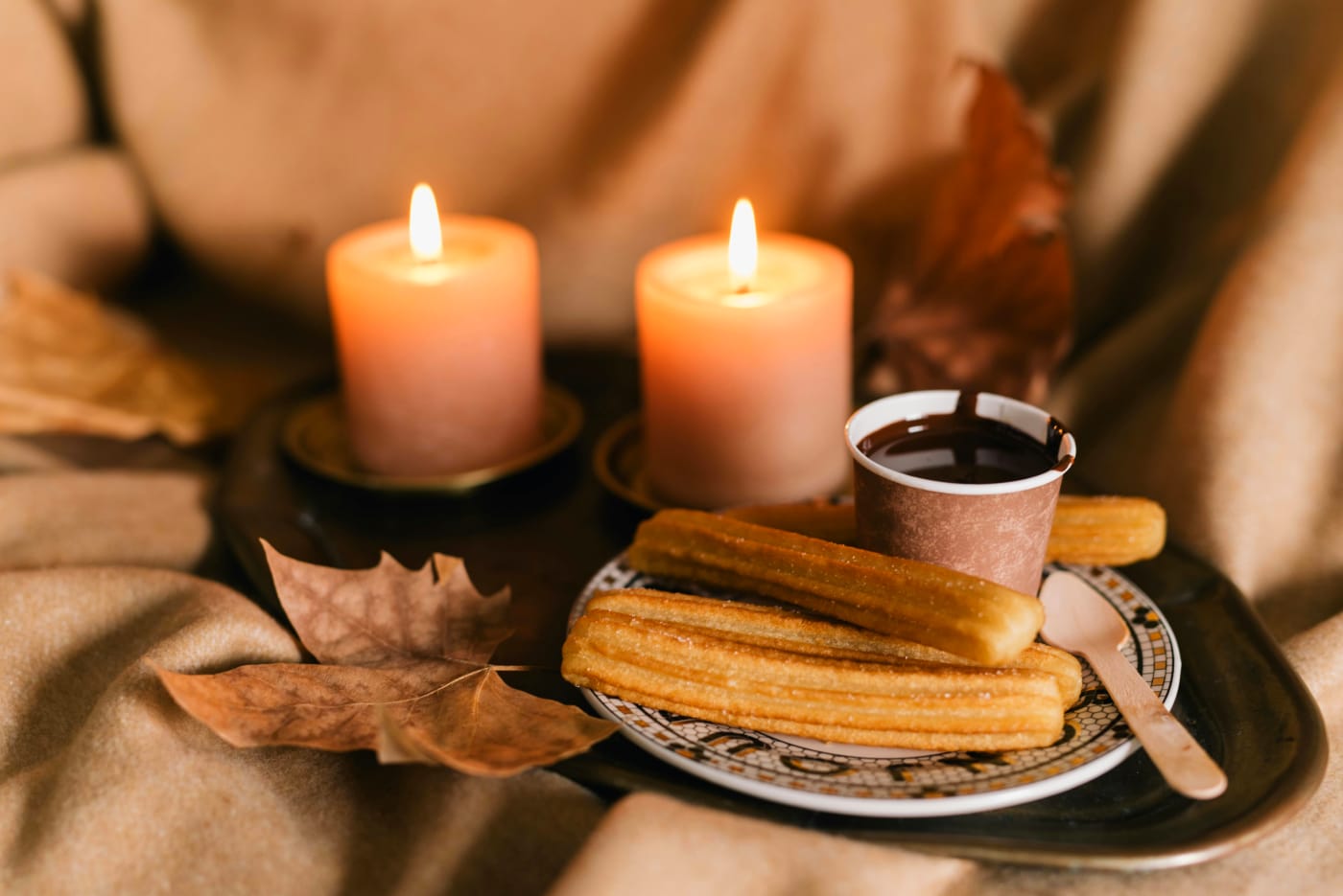 Spanish churros served with hot chocolate and surrounded by lit candles on a rustic tray, ideal for a festive dessert menu.