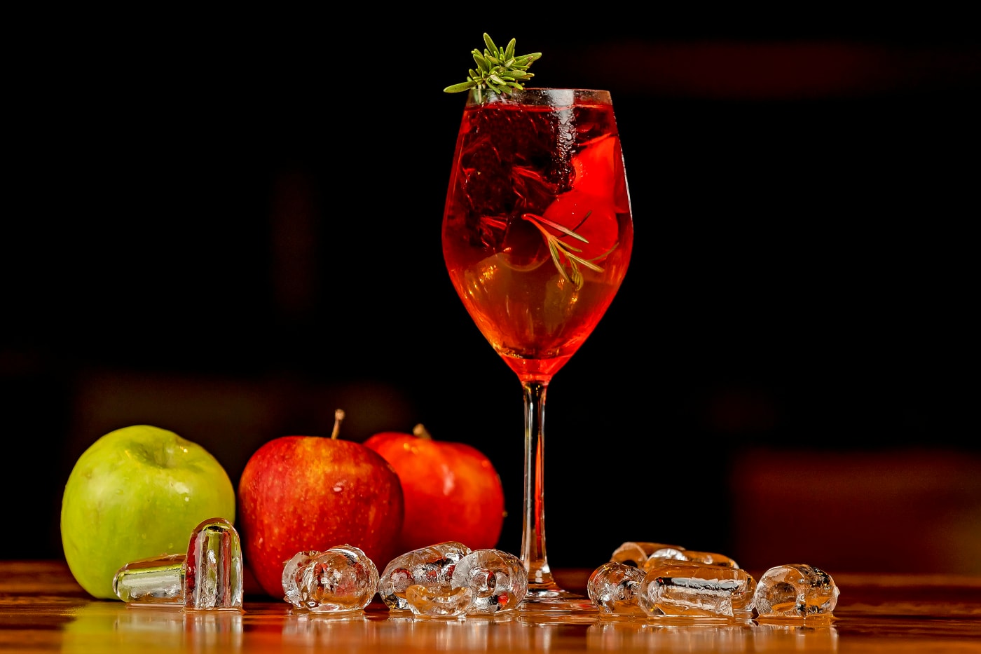A glass of traditional sangria with fruit slices and ice cubes, surrounded by fresh apples and ice on a table, perfect for a festive occasion.