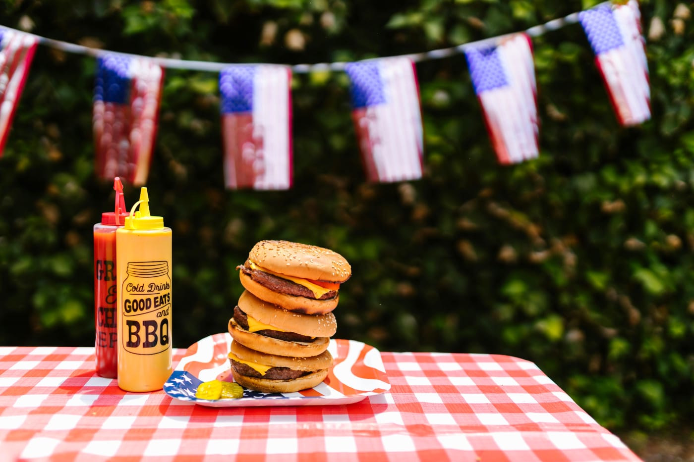 Burgers and BBQ sauces on a picnic table, ready for an American theme party with red, white, and blue decorations.