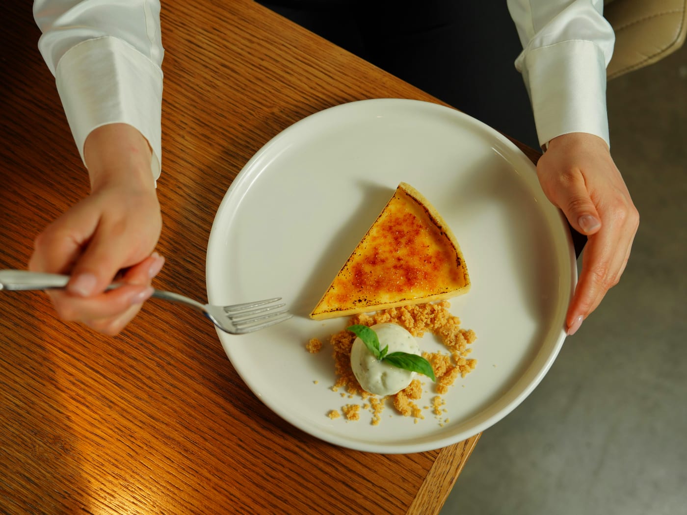 Person enjoying a creme brulee with a perfect caramelized crust, served with garnish and crumbled base.