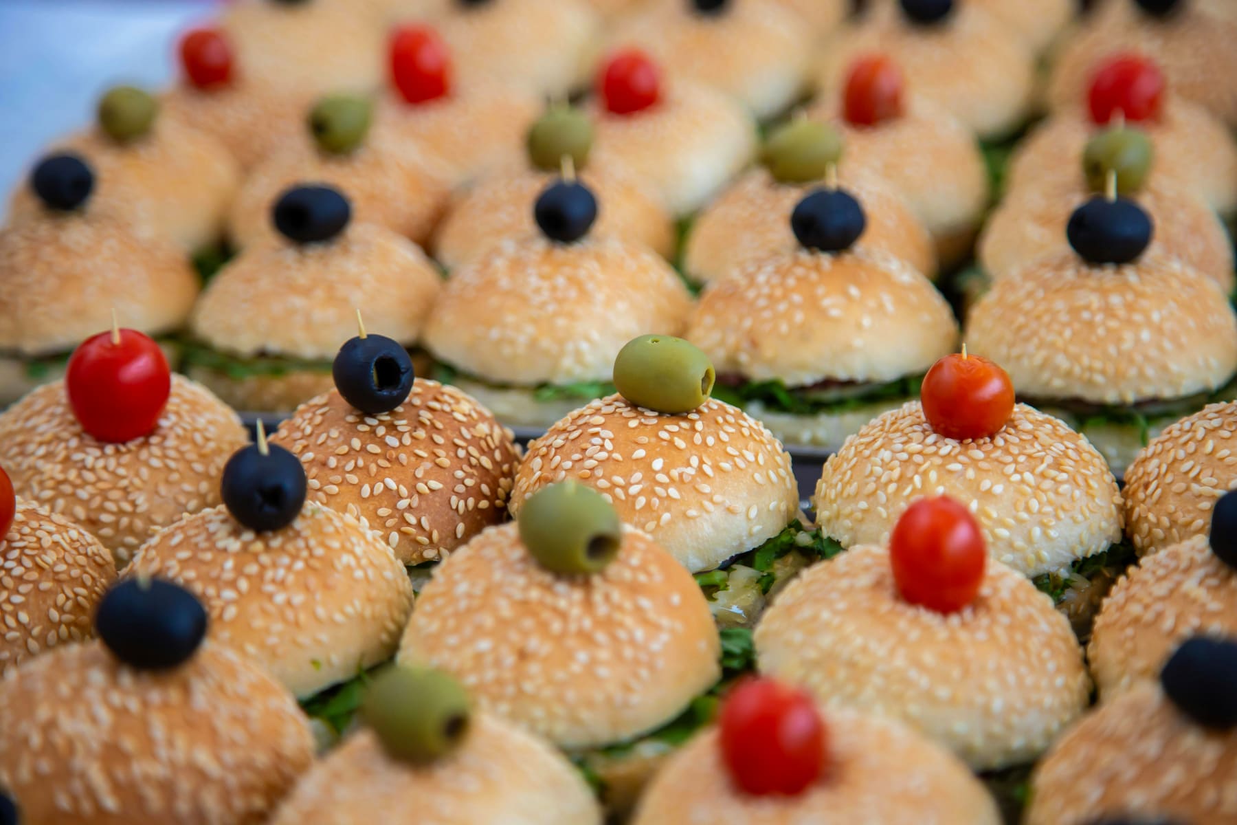 Festive appetizers with mini sandwiches adorned with black olives and flower in elegant settings for a party.