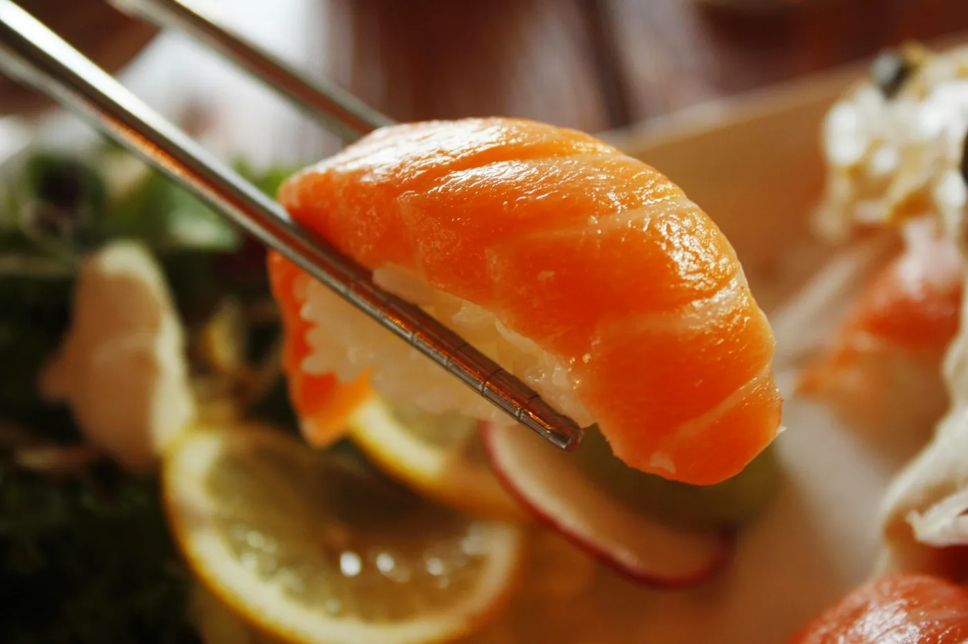 Tæt på et stykke røget laks holdt med spisepinde, ledsaget af citronskiver og salat, perfekt til traditionelle forretter.