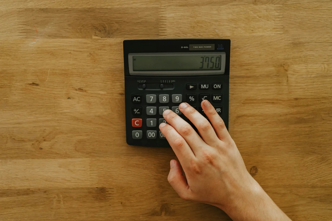 Hand using budget calculator on wooden table for confirmation planning.
