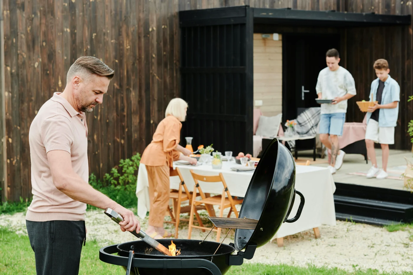 Mænd og kvinder nyder Sankt Hans aften ved grillen, med fokus på samvær og lækker grillmad.