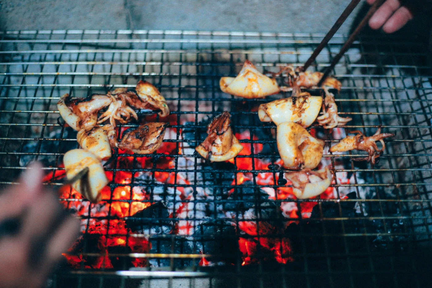 Personer griller kyllingestykker på en kulgrill med synlige glødende kul, der skaber en autentisk grilloplevelse.