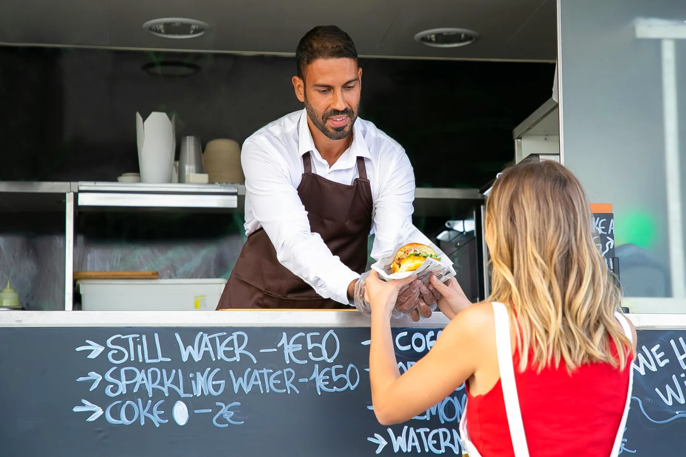 Street food vendor serving diverse street food from a food truck, with menu signage.
