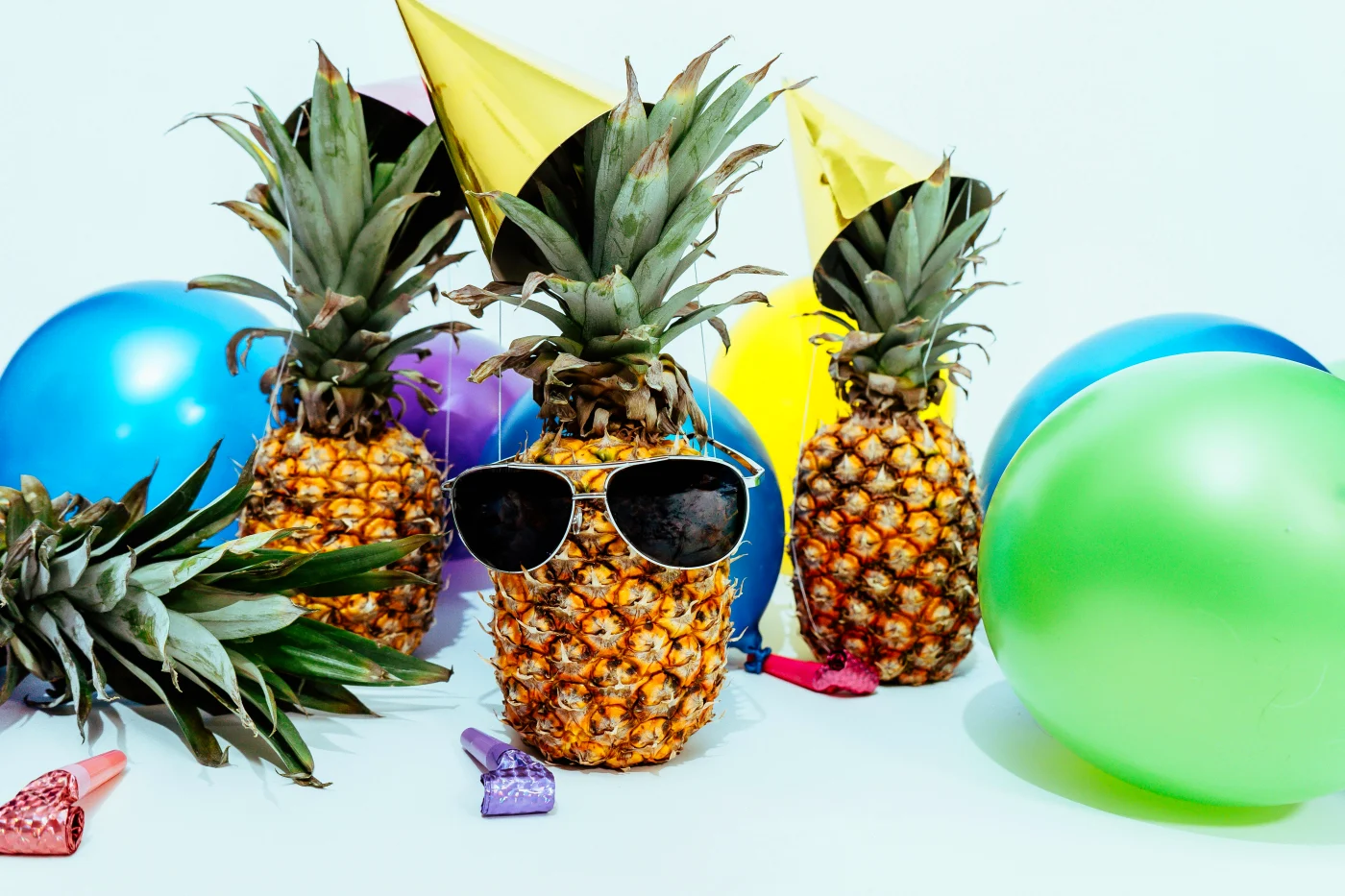 Colorful pineapples with sunglasses and festive hats surrounded by balloons, capturing the lively atmosphere of a street food party.