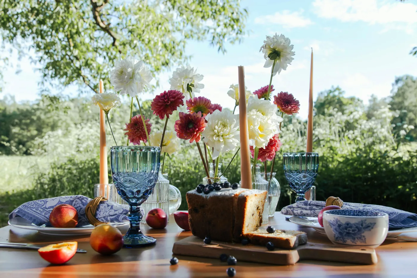 Udendørs luksuriøs borddækning med blomster, stearinlys og gourmetretter, ideel til en elegant sommerfest.