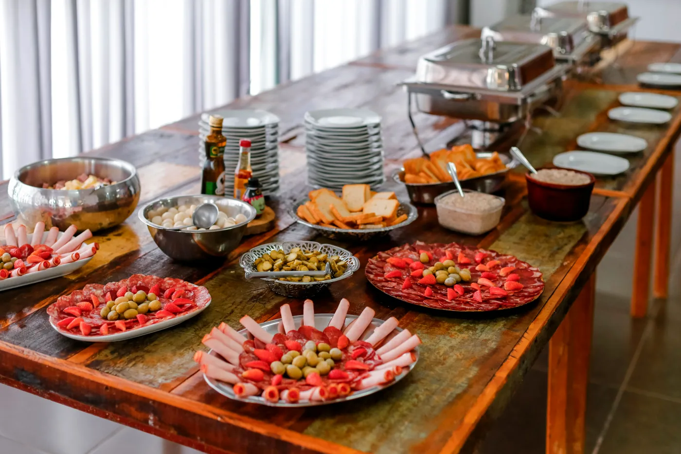 Bord med diverse buffetretter, der illustrerer cateringmuligheder til festplanlægning. Retterne inkluderer forskellige slags kød og oliven, der præsenteres professionelt på fade, perfekt til overvejelser om catering versus hjemmelavet mad.