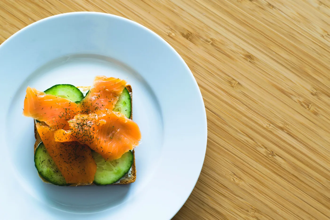 Traditional Danish open-faced sandwiches with smoked salmon and cucumbers on rye bread, served on a white plate.