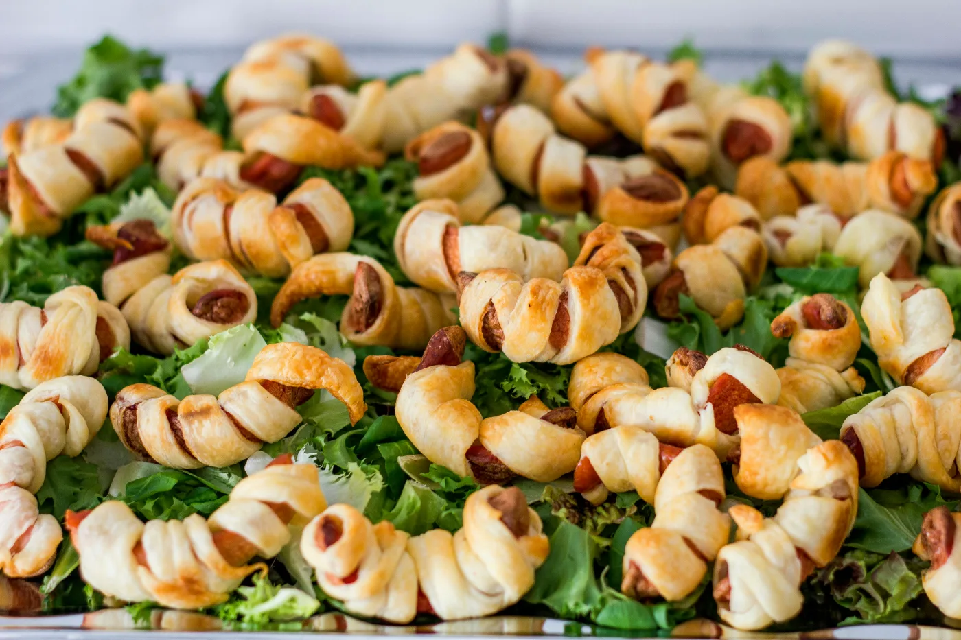 Tasty sausage rolls with golden puff pastry, served on a green salad platter, perfect for festive gatherings and late-night food.