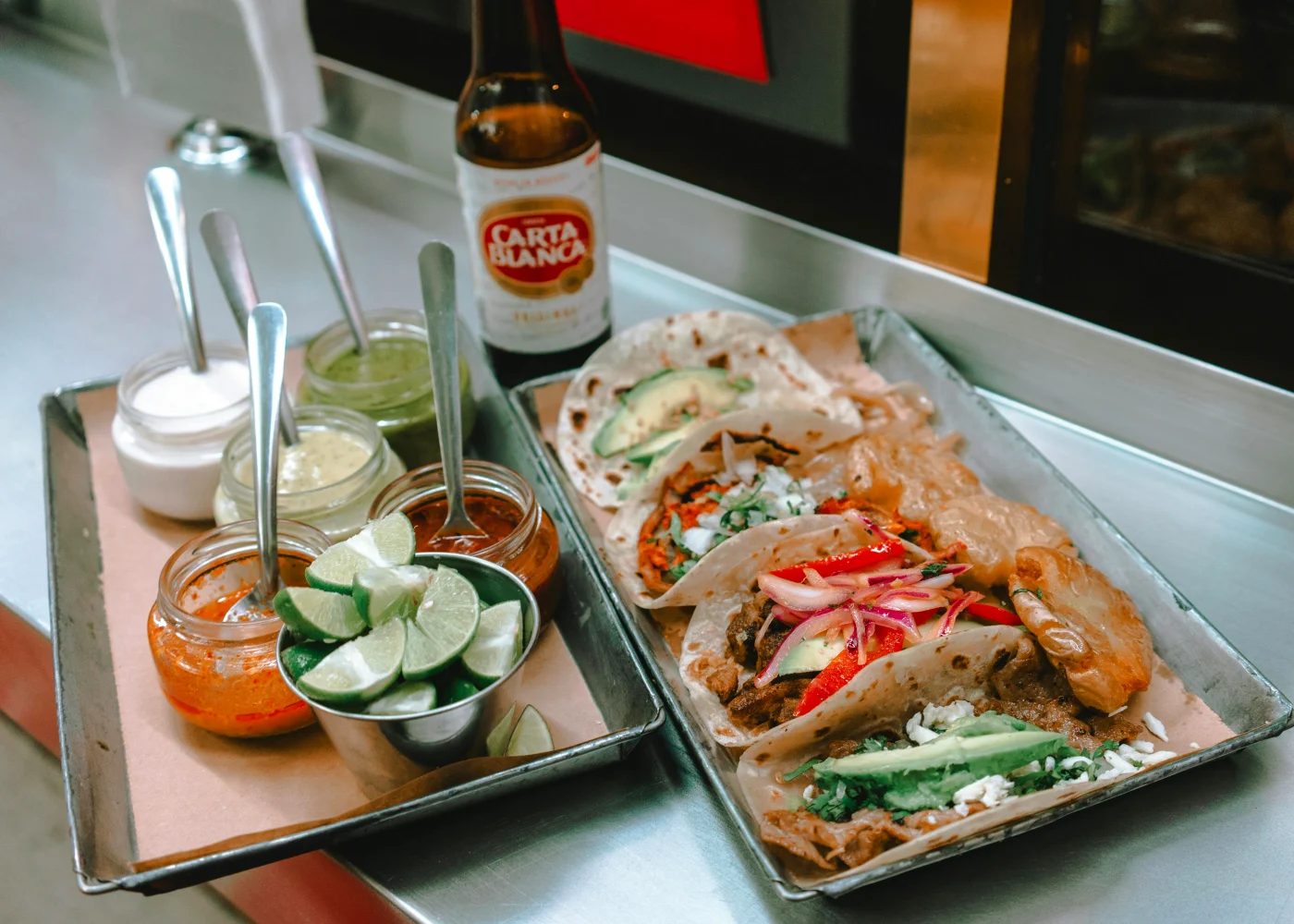 Enticing tacos with an assortment of toppings like lime, salsa, and guacamole, served with a beer for a festive late-night snack.
