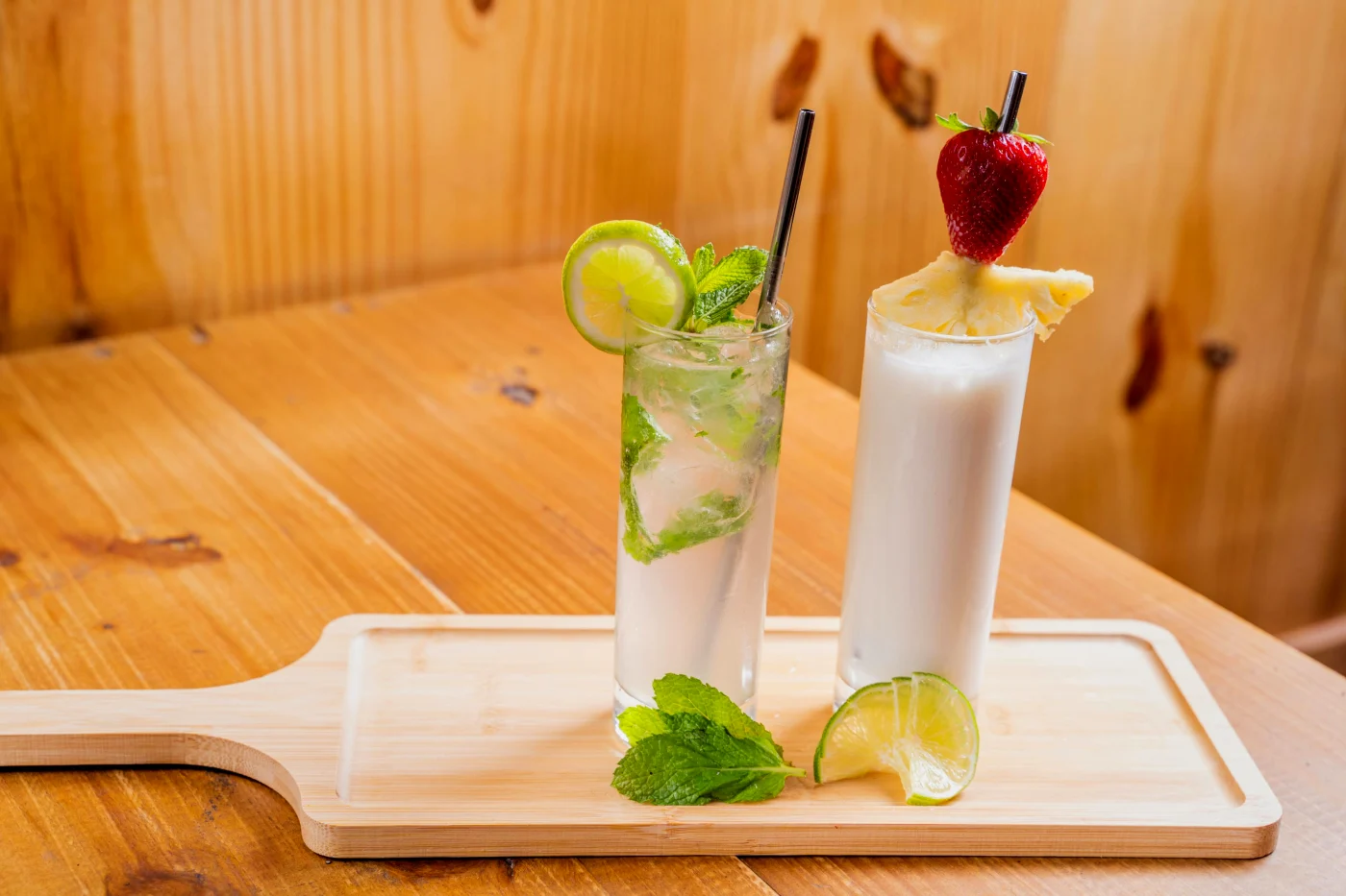 A tropical pina colada with pineapple slice and strawberry as garnish, served on a wooden board.
