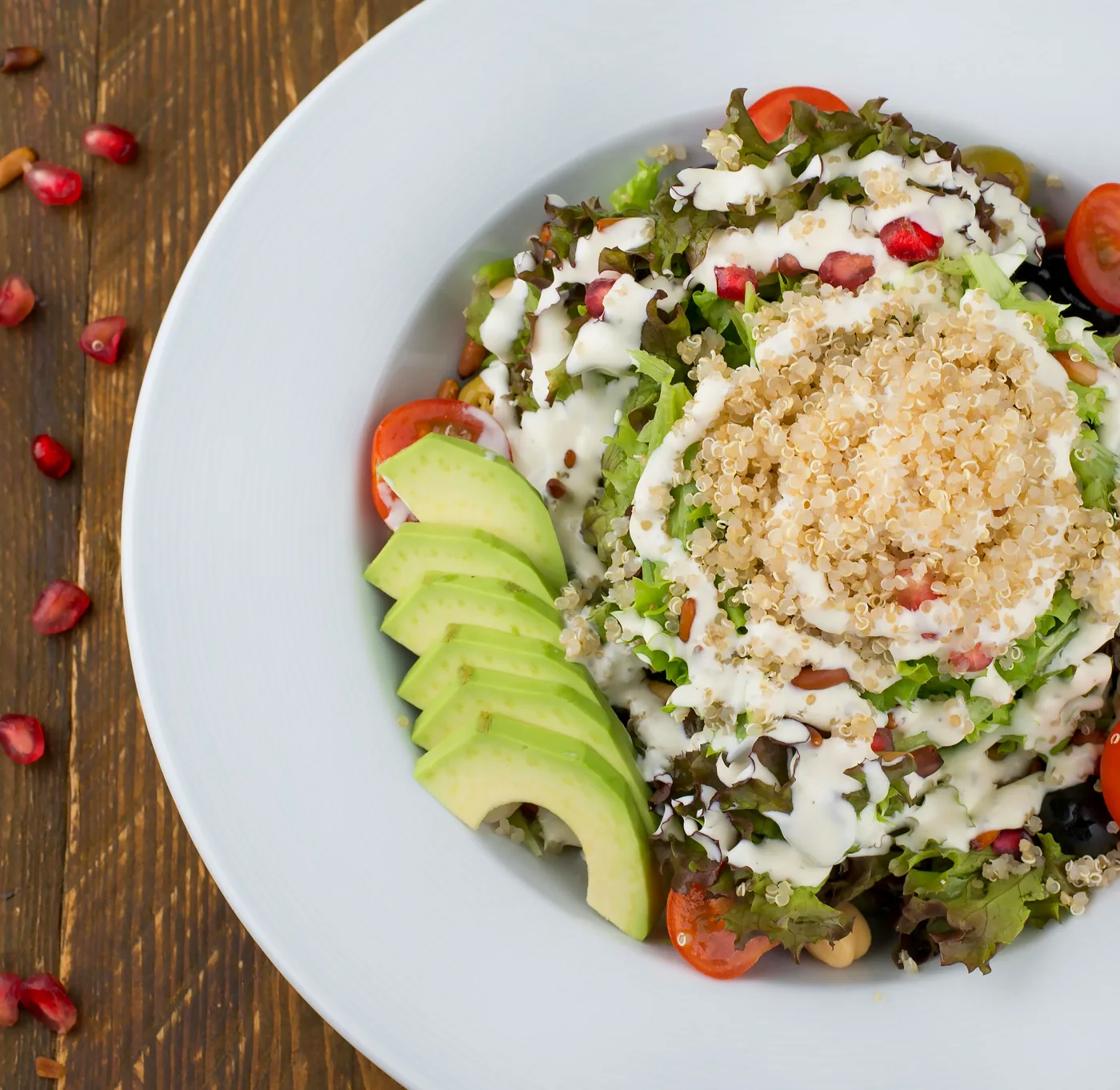 Farverig quinoa-salat med granatæble, cremet feta og friske grøntsager på en hvid tallerken, der fremhæver salatens sunde og moderne ingredienser.