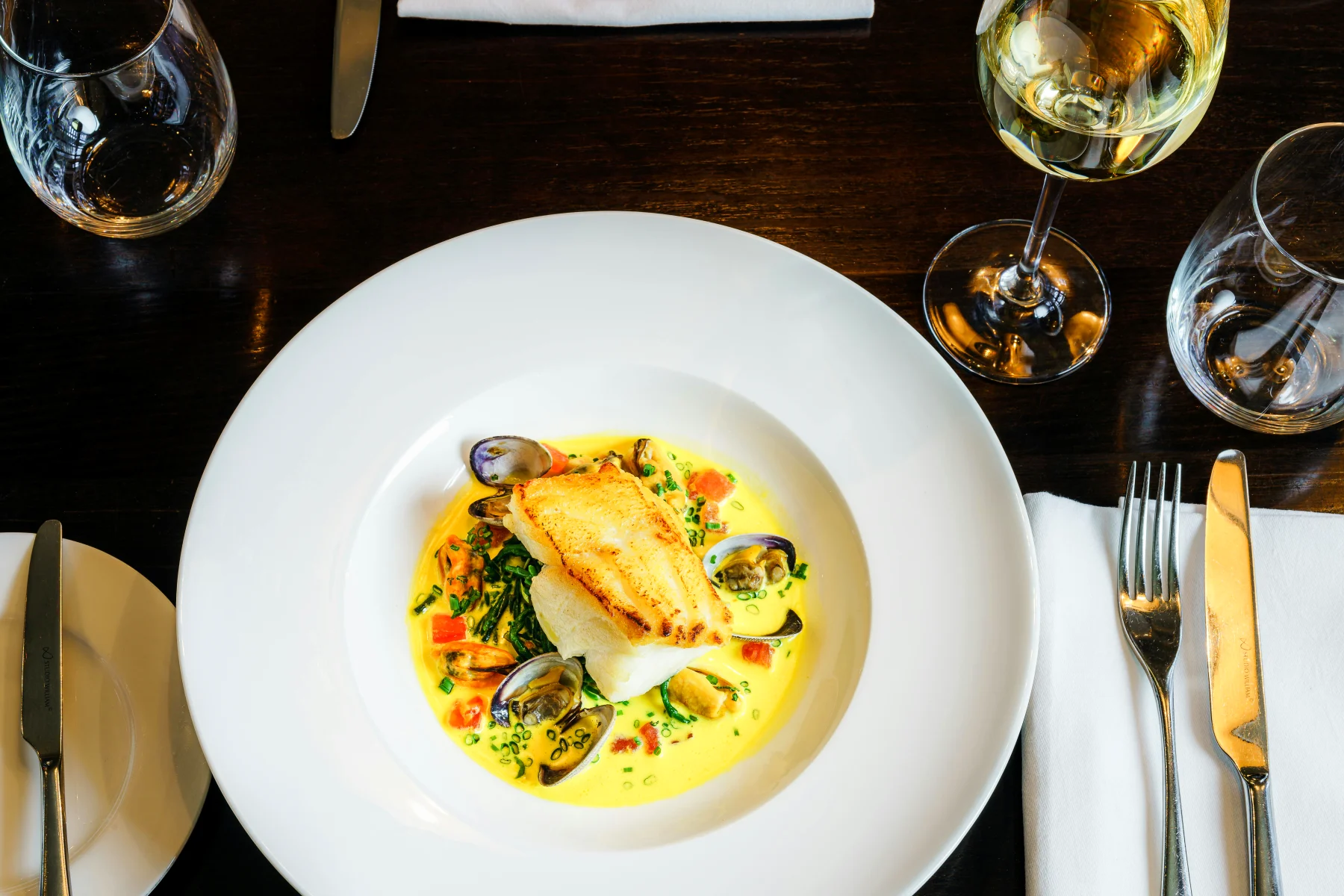 Delicately arranged fish dish with shellfish and herbs on an elegant plate, reflecting the theme of seafood menus in the article.