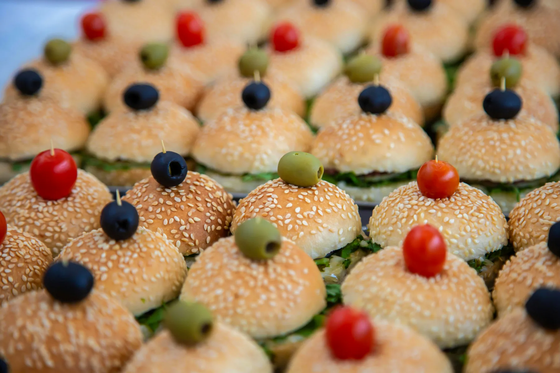 Festive appetizers with mini sandwiches adorned with black olives and flower in elegant settings for a party.