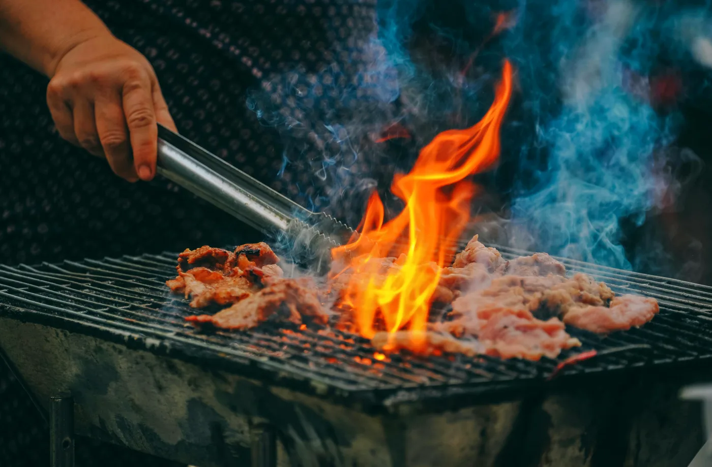 Kok griller saftigt kød over åben ild, mens duften fylder luften, perfekte kulinariske oplevelser til DHL Stafetten med ChefMe.