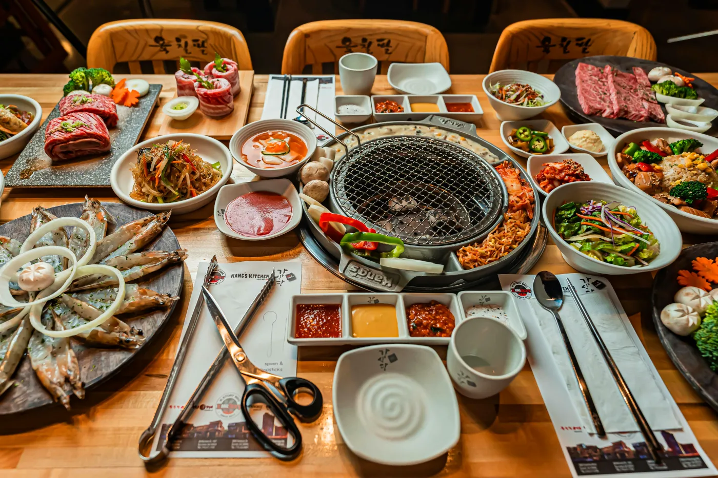 A beautifully set dinner with different meat dishes and colorful side dishes such as vegetables and salads around a grill.