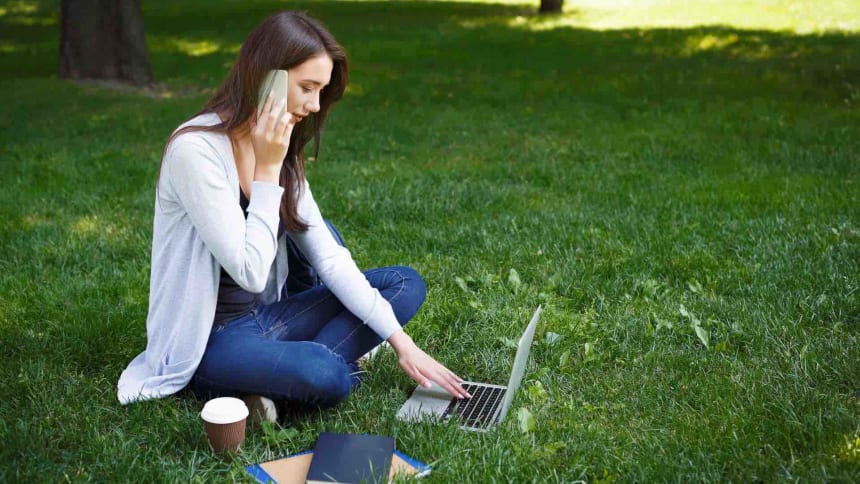 Frau_im_Park_auf_Rasen_sitzend_mit_Smarthphone_und_Notebook
