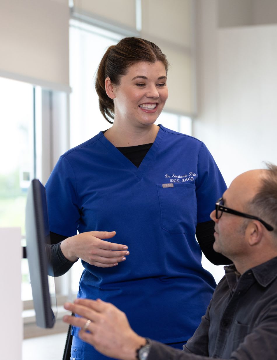 A dental team member in blue scrubs chatting with a patient